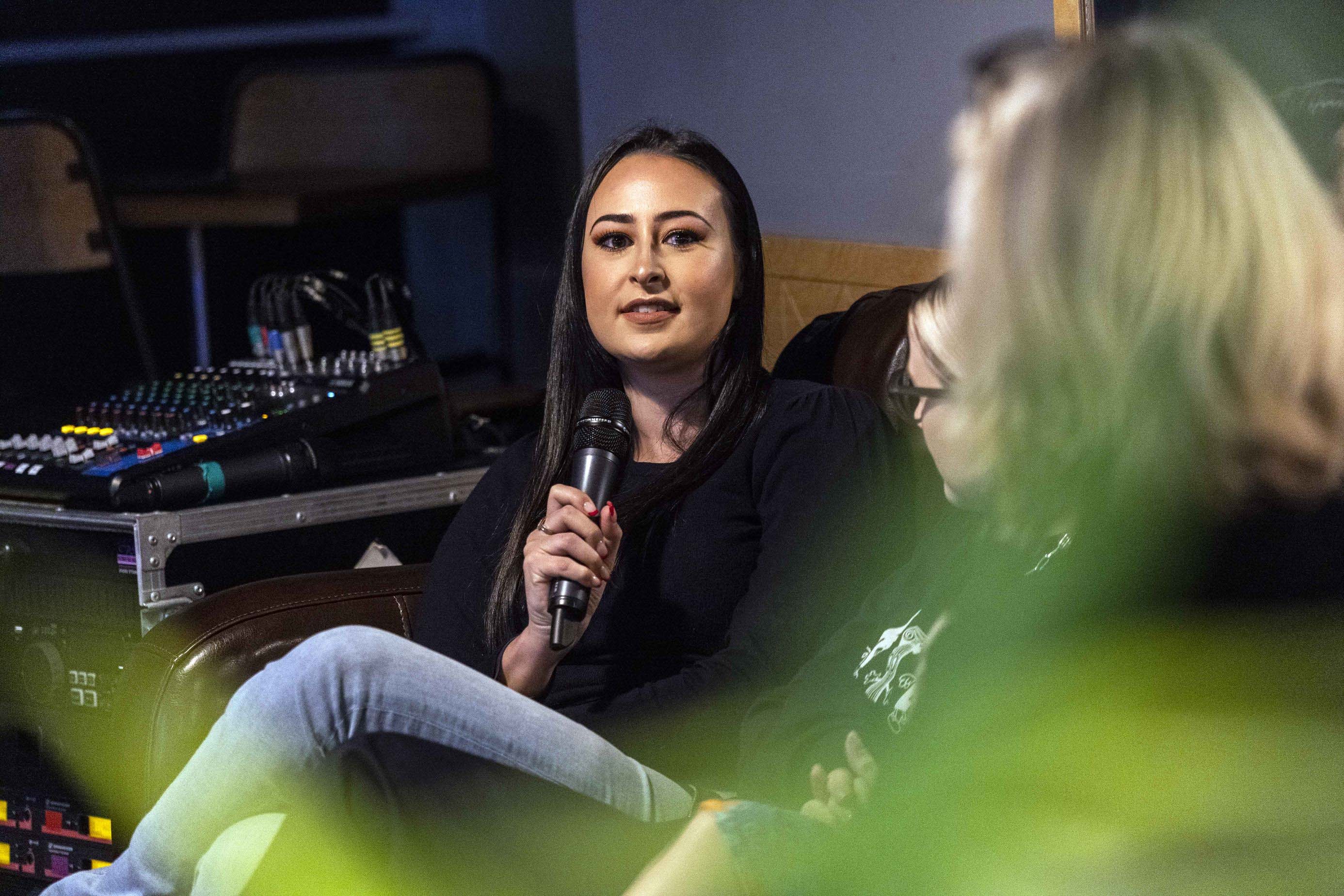A woman at a panel discussion holding a microphone. In the background is sound equipment