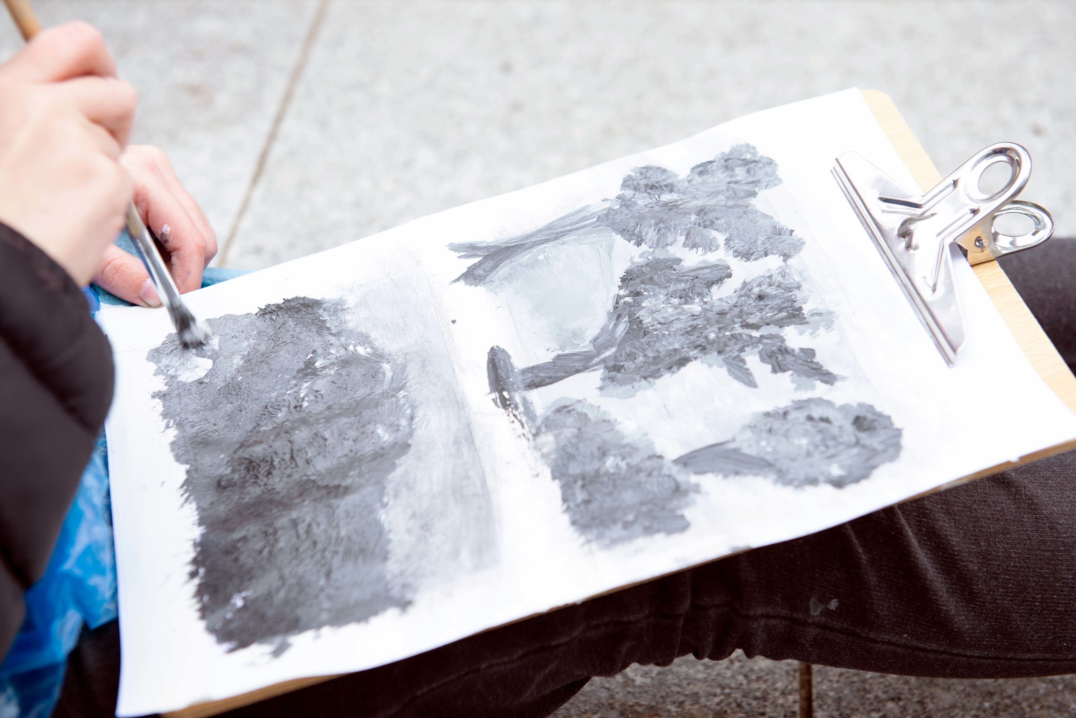 A person paints in grey paint on a piece of paper attached to a clipboard.
