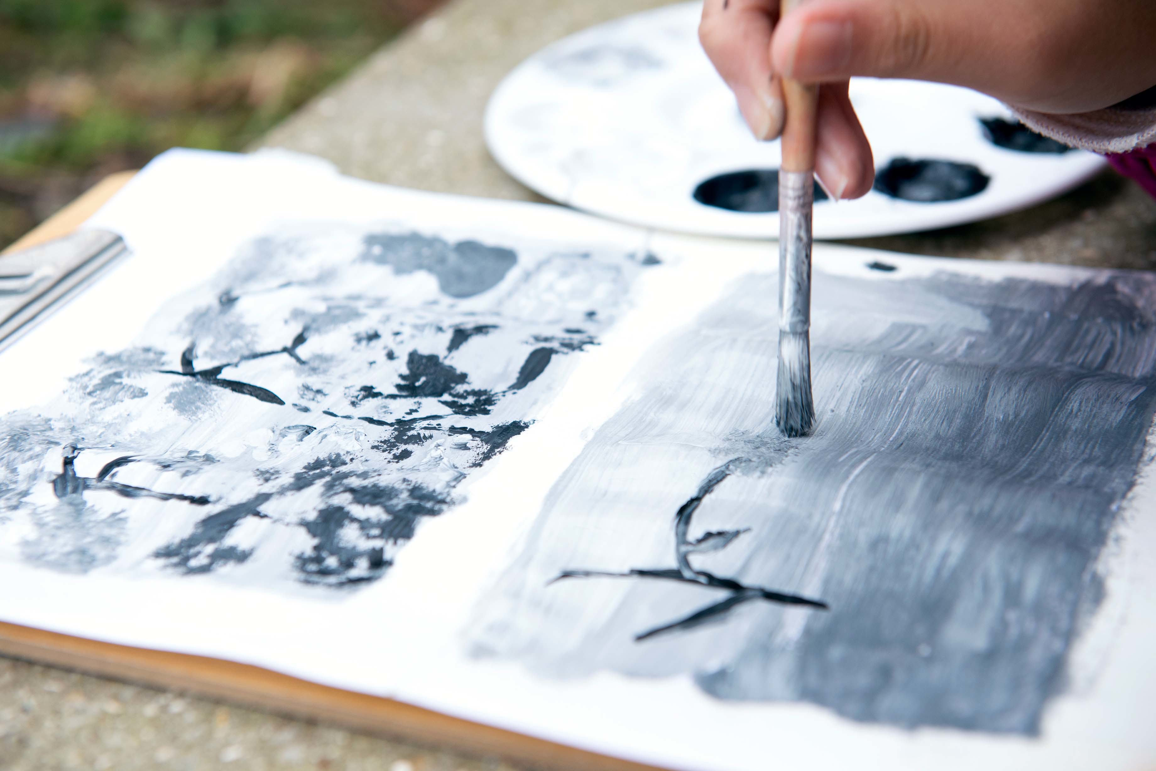 A person painting horizontal strokes on a piece of paper attached to a clipboard.