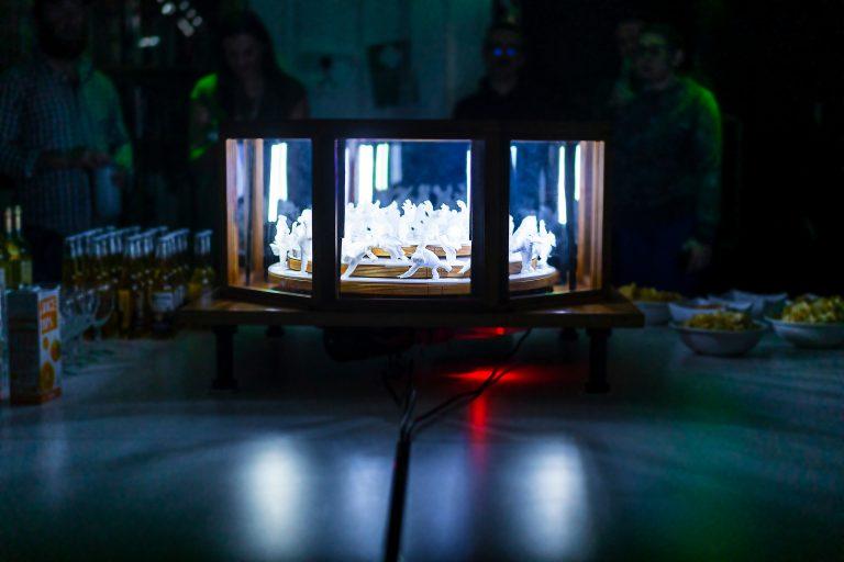 Rows of figures in a lit-up octagonal box, sitting on a table.