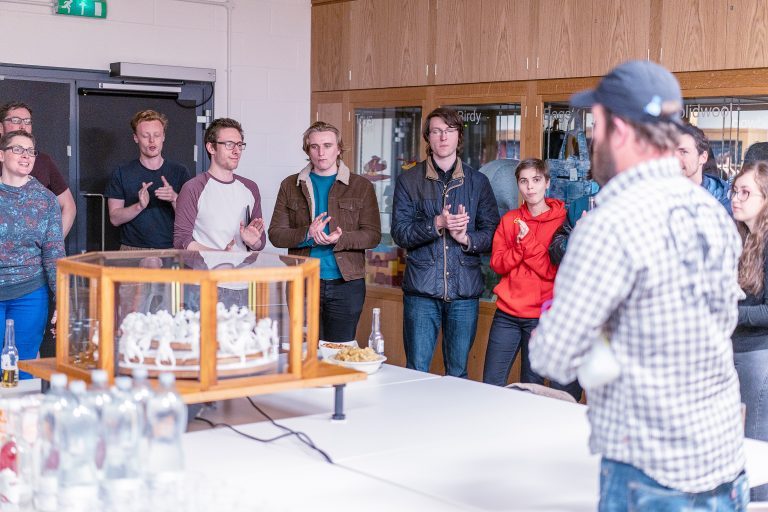 A group of people applauding in front of a table with a large octagon-shaped box on it.