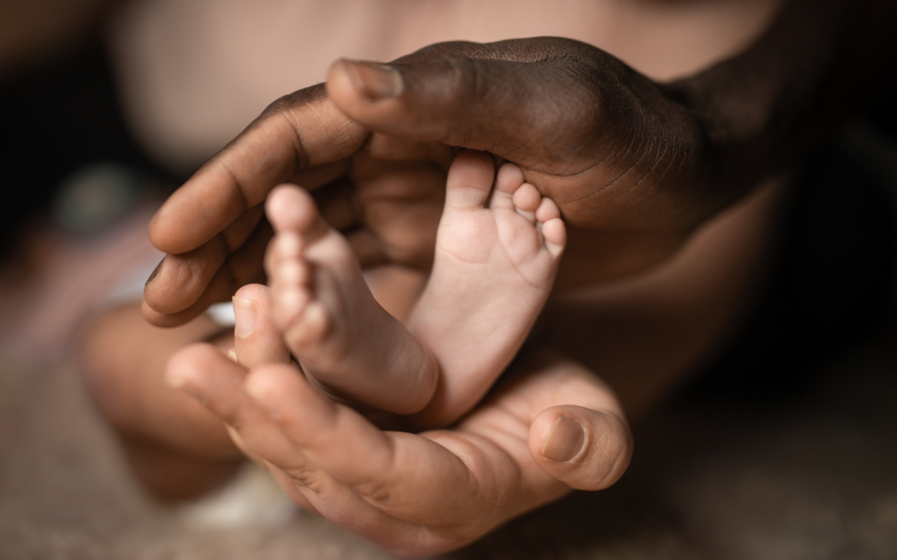 The hands of a mother and father surround the tiny feet of their baby