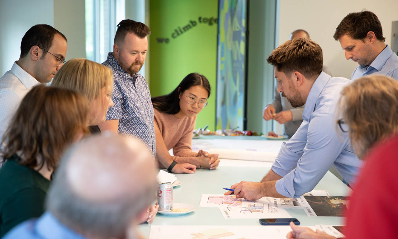 A group of people are sitting around a table looking at a map. Description generated by AI