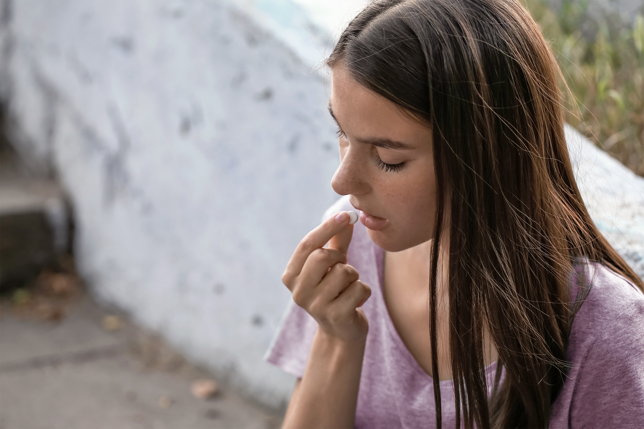 Close-up of a young woman taking a tablet outdoors, to illustrate information about drug use and women’s bodies.