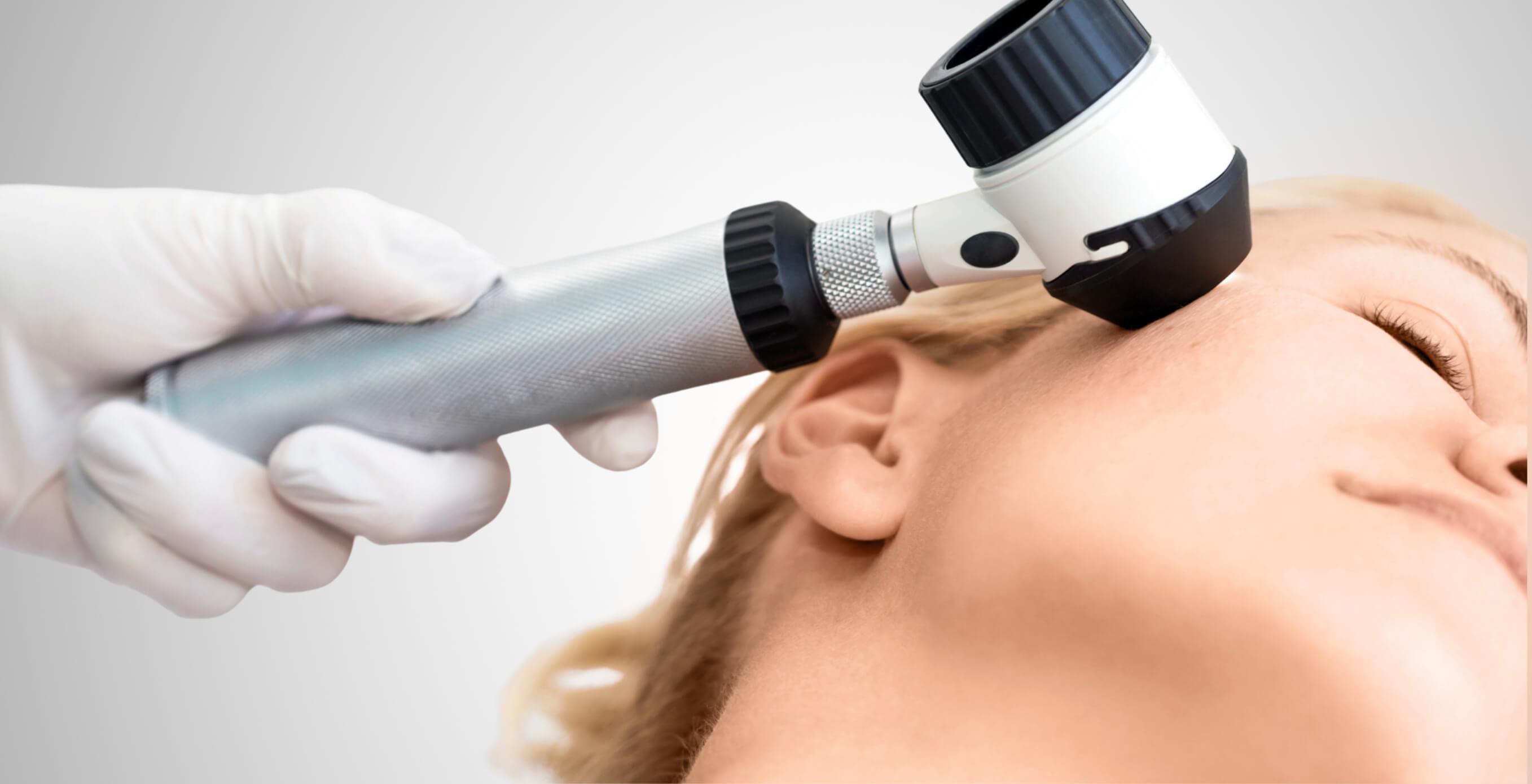 Auf dem Bild ist eine dermatologische Untersuchung zu sehen: Eine Fachärztin oder ein Facharzt betrachtet die Haut im Gesicht einer Patientin mithilfe eines Dermatoskops – einem speziellen Vergrößerungsgerät zur präzisen Beurteilung von Hautveränderungen. Solche Untersuchungen sind essenziell, um eine bakterielle Hauterkrankung frühzeitig zu erkennen und gezielt zu behandeln. Bei Dermacare Wien erfolgt die Diagnose stets unter ärztlicher Aufsicht und mit modernster Technologie, um Entzündungen, Infektionen oder andere Hautprobleme präzise zu bestimmen und individuell zu therapieren.