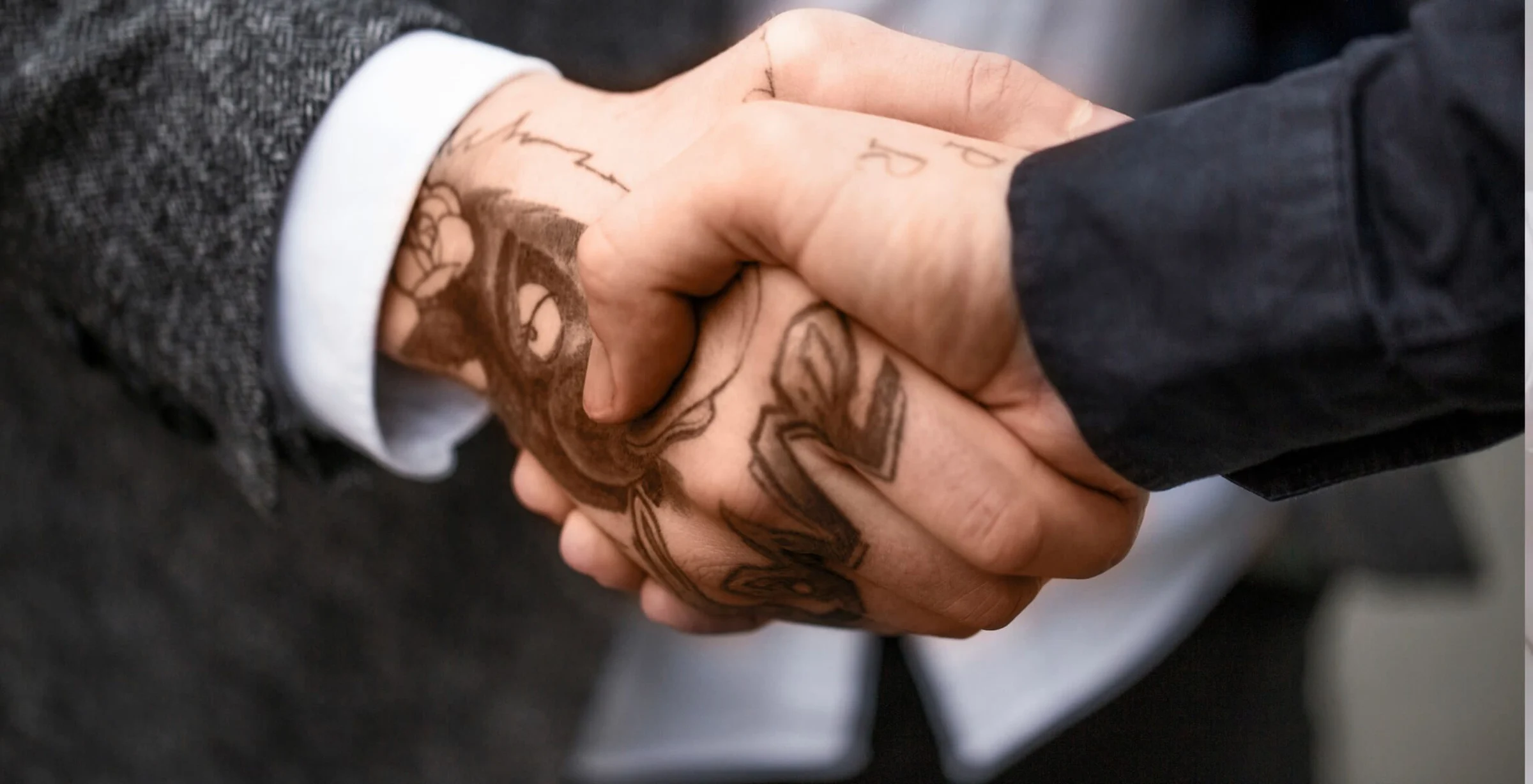 Auf dem Bild sieht man wie Tattoos im Job auch hin und wieder akzeptiert werden können. Zwei personen mit Tattoos auf der Hand schütteln sich die Hand.
