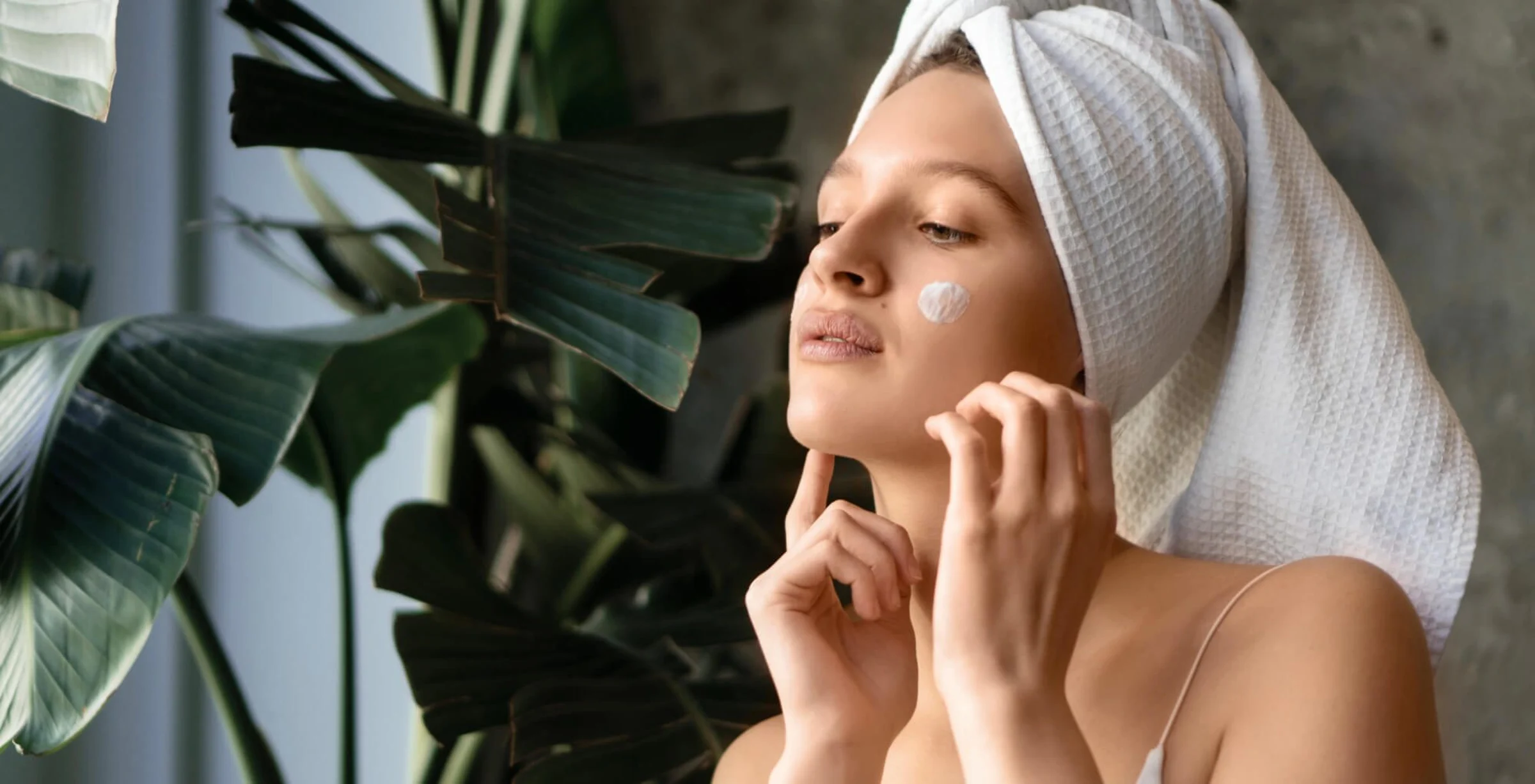 Eine junge Frau mit Handtuchturban trägt sanft eine Pflegecreme auf ihr Gesicht auf. Die Szene vermittelt Frische und Entspannung – perfekt als Symbol für intensive Gesichtspflege und nachhaltige Tiefenreinigung im Sommer. Das Bild passt ideal zum Thema Aquafacial bei Dermacare Wien, das die Haut porentief reinigt und mit Feuchtigkeit versorgt.