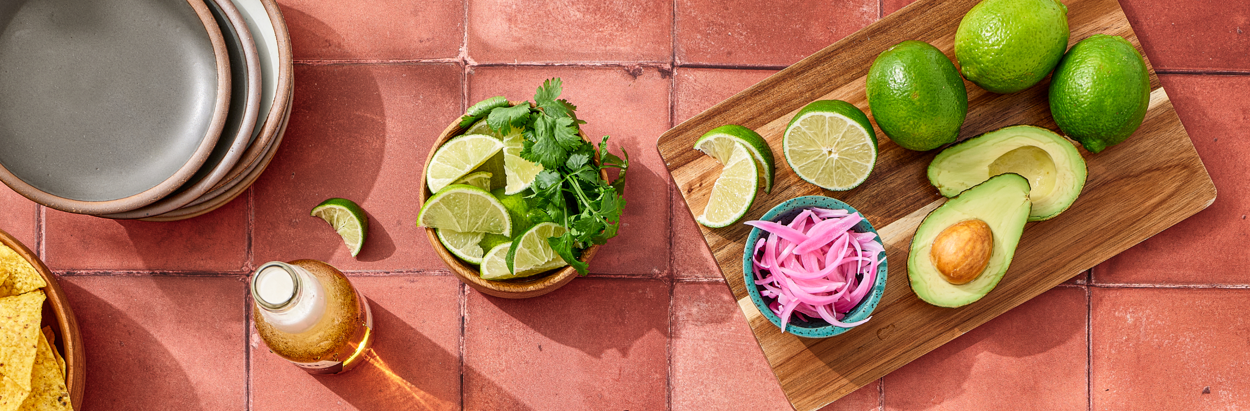 Fresh limes, pickled onions, avocado, and cilantro on a tiled table