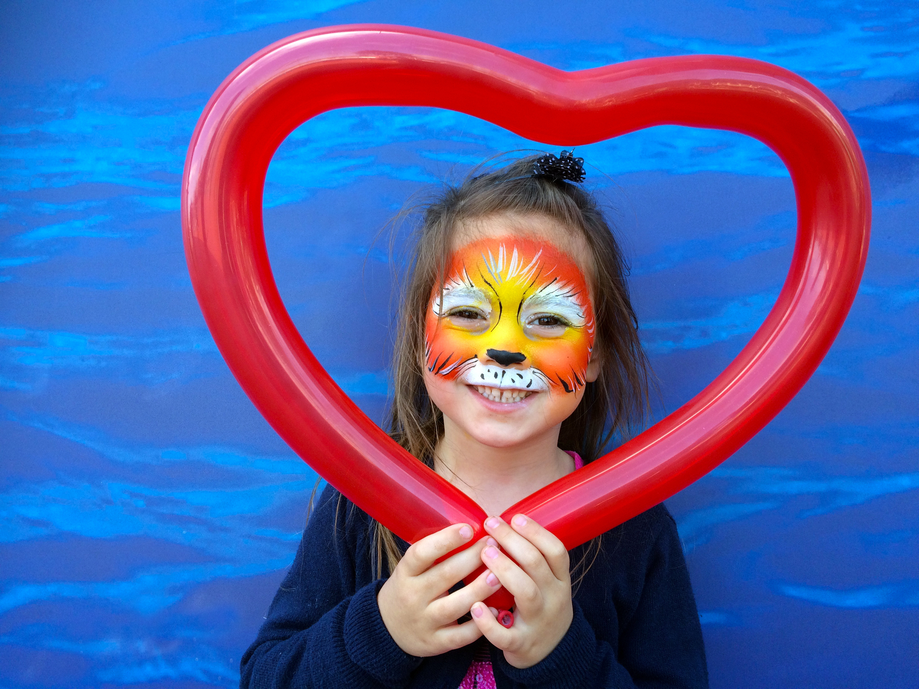 Little child (girl age 5-6)  with lion face painting  holding balloon in a shape of heart