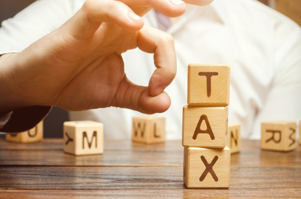 View of hand about to flick away a stack of wooden blocks spelling the word Tax.