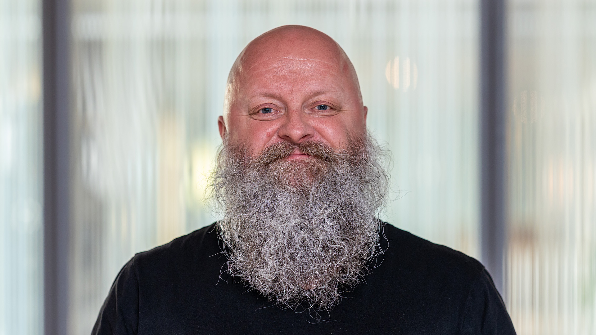 Foto. Mann med skjegg ser i kamera og smiler