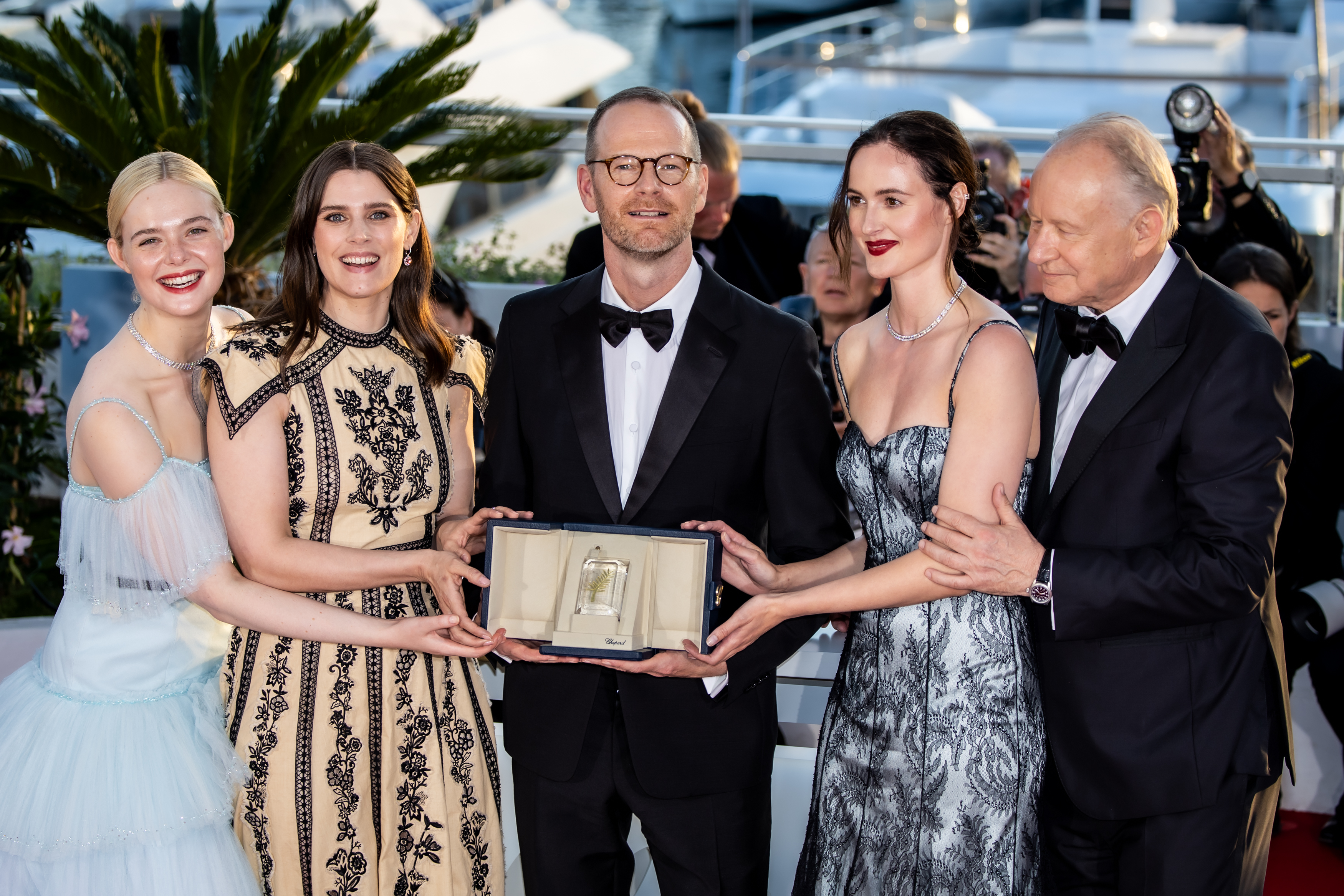 foto. fem personer i festklær står samlet rundt et pristrofe utendørs med Joachim Trier i midten
