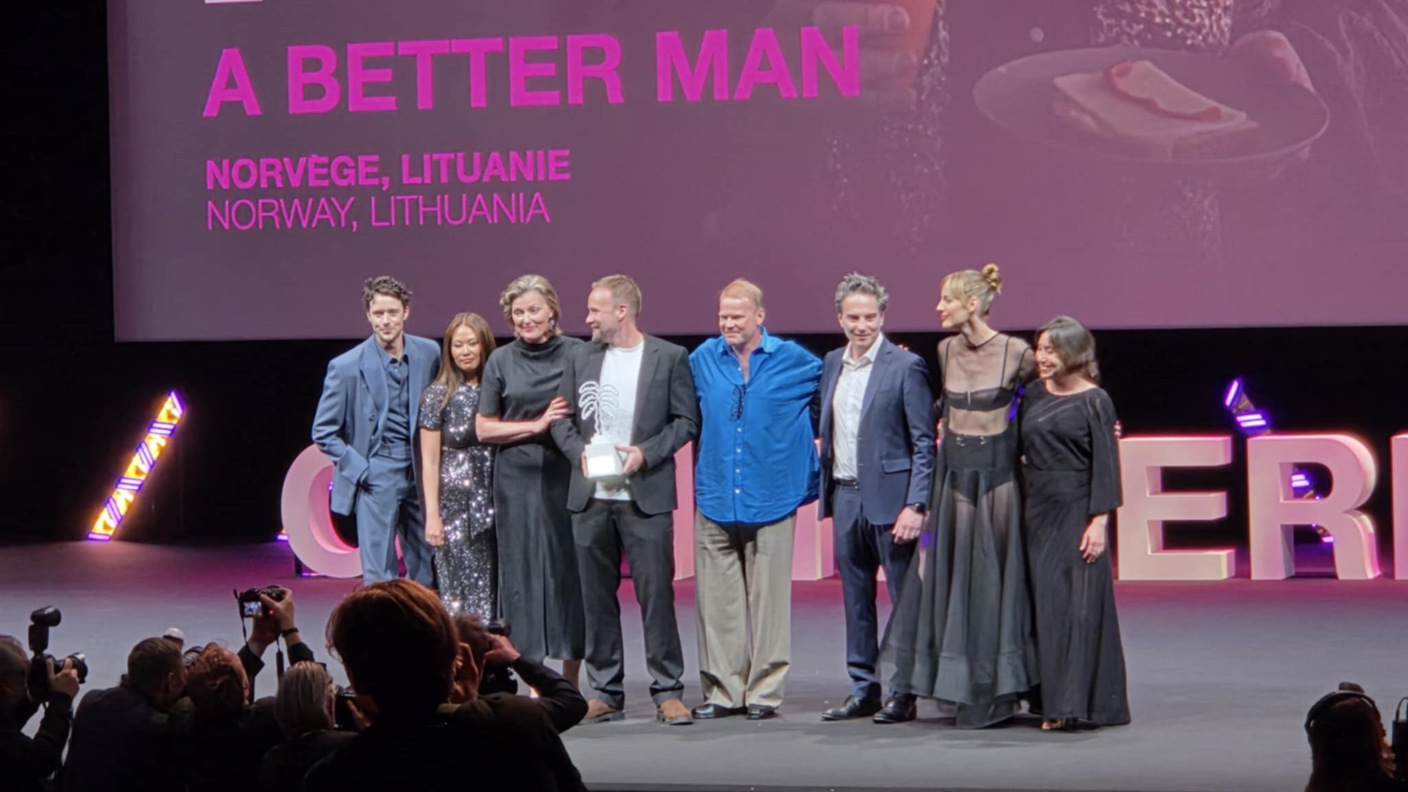 Foto. Menn og kvinner i fine klær foran lerret mottar applaus.