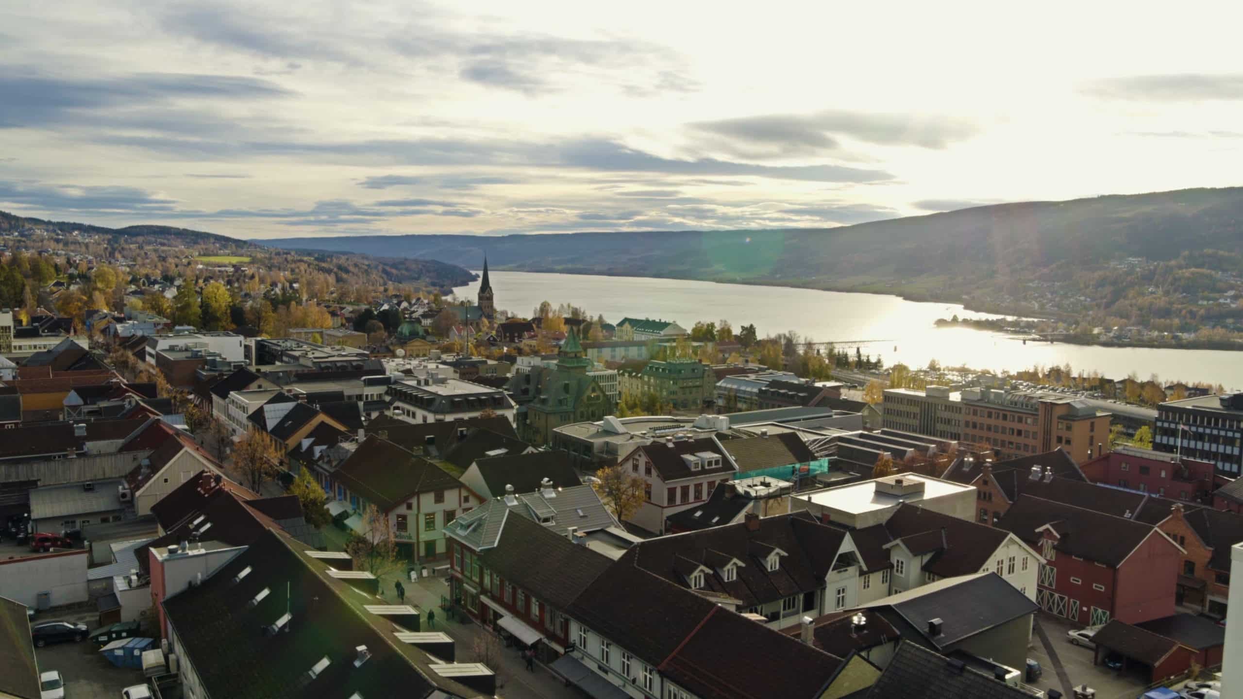 foto. Oversiktsbilde over en by, med tak og kirke, Sjø og fjell i bakgrunnen