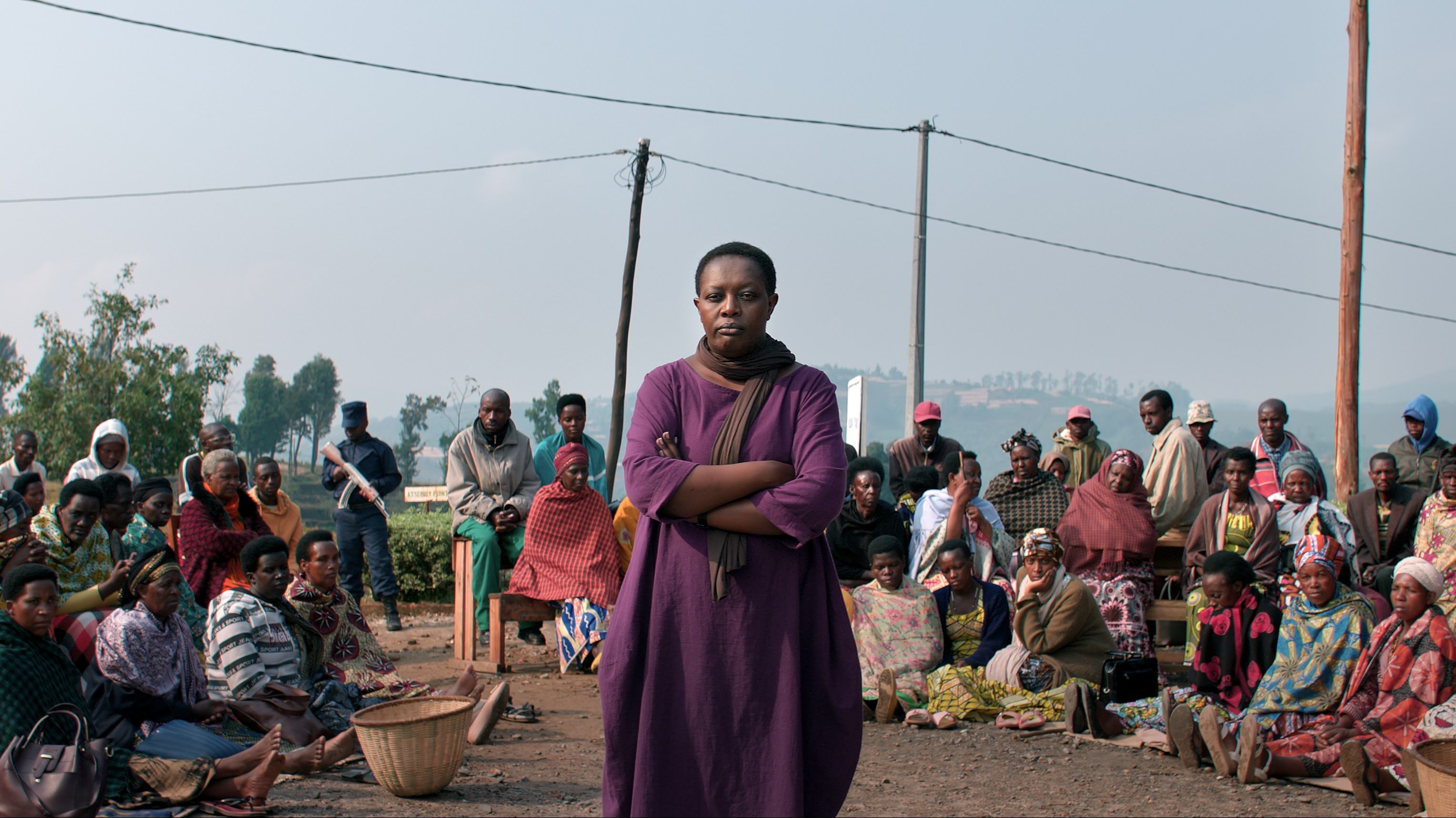 Kvinne i lilla kjole står et sted i Afrika og blir sett på av en større gruppe mennesker bak henne.