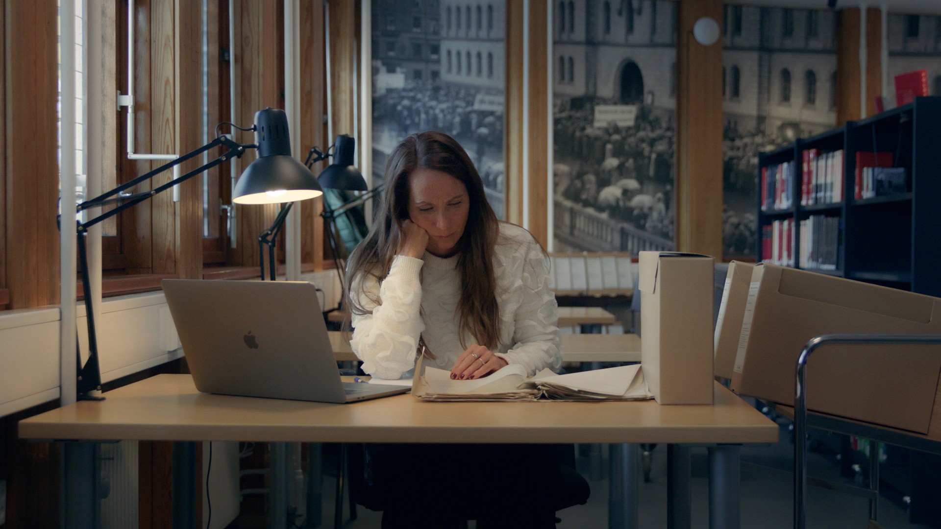 Foto. En kvinne sitter på et kontor og leser på noen papirer