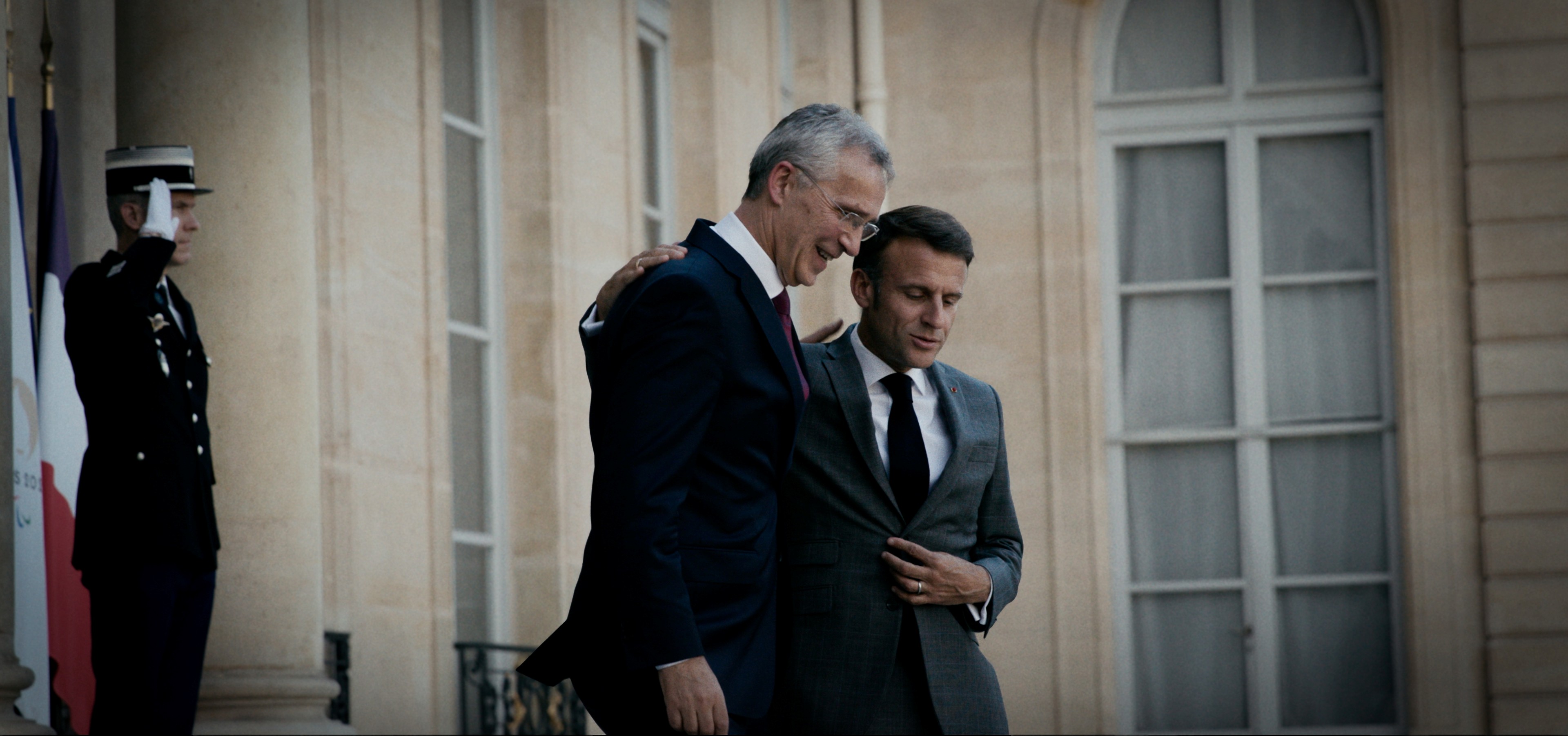 Jens Stoltenberg og Emanuel Macron på vei ned en trapp mens de holder rundt hverandres skuldre.