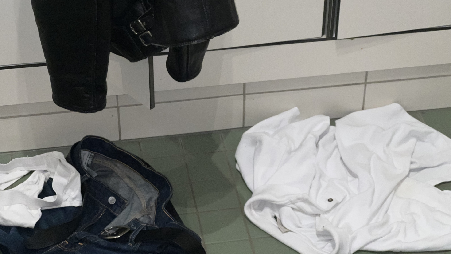 en svart bukse, en hvit skjorte og en hvit underbukse ligger slengt på et garderobegulv under en svart jakke