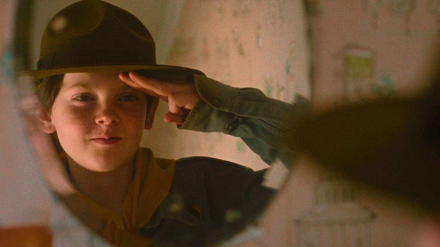 Foto.En ung gutt i speideruniform ser på seg selv i speilet mens han tar en speiderhilsen