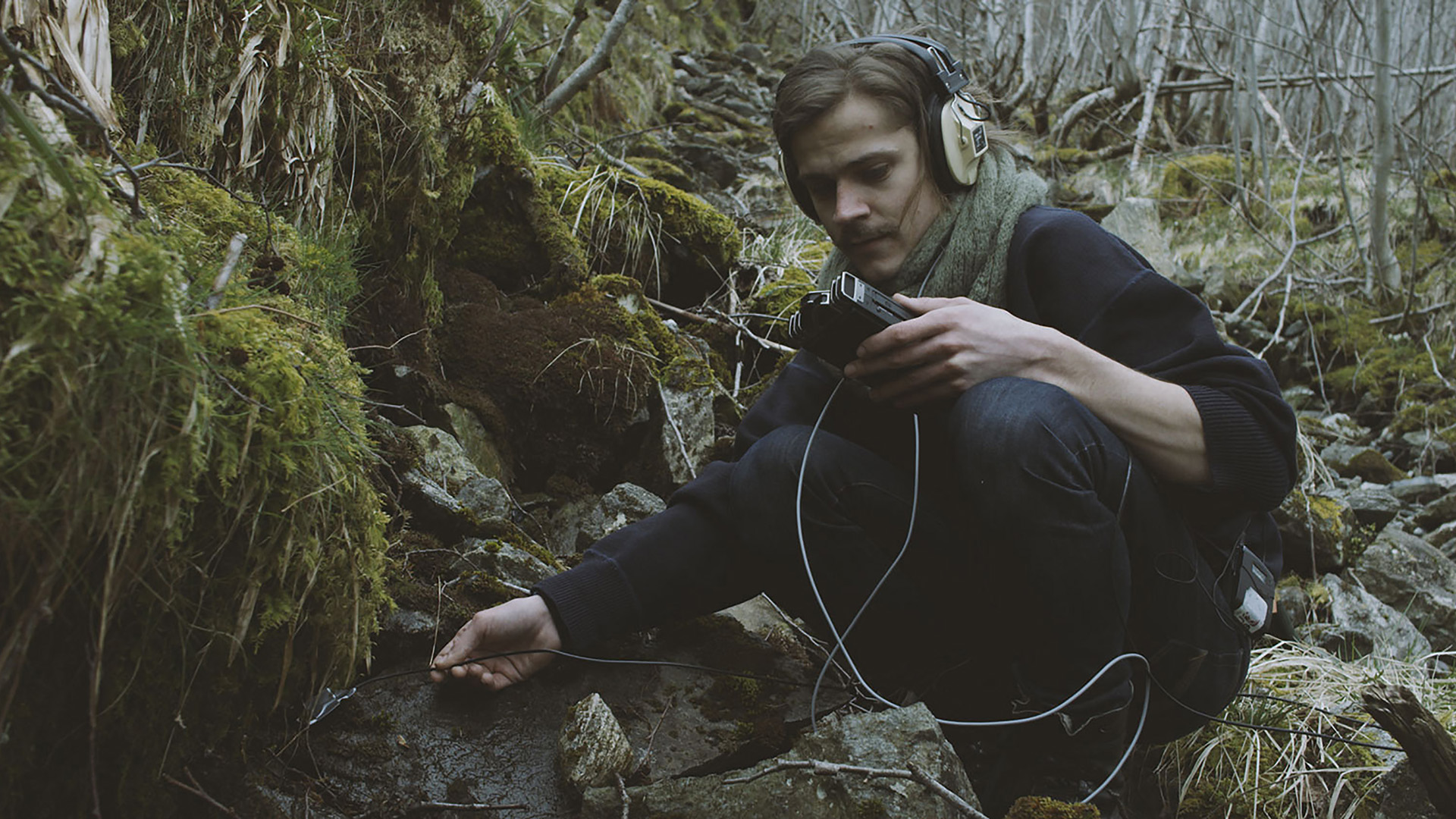 Foto.Ung mann sitter ute i skogen med opptaksutstyr og tar opp lyder fra naturen