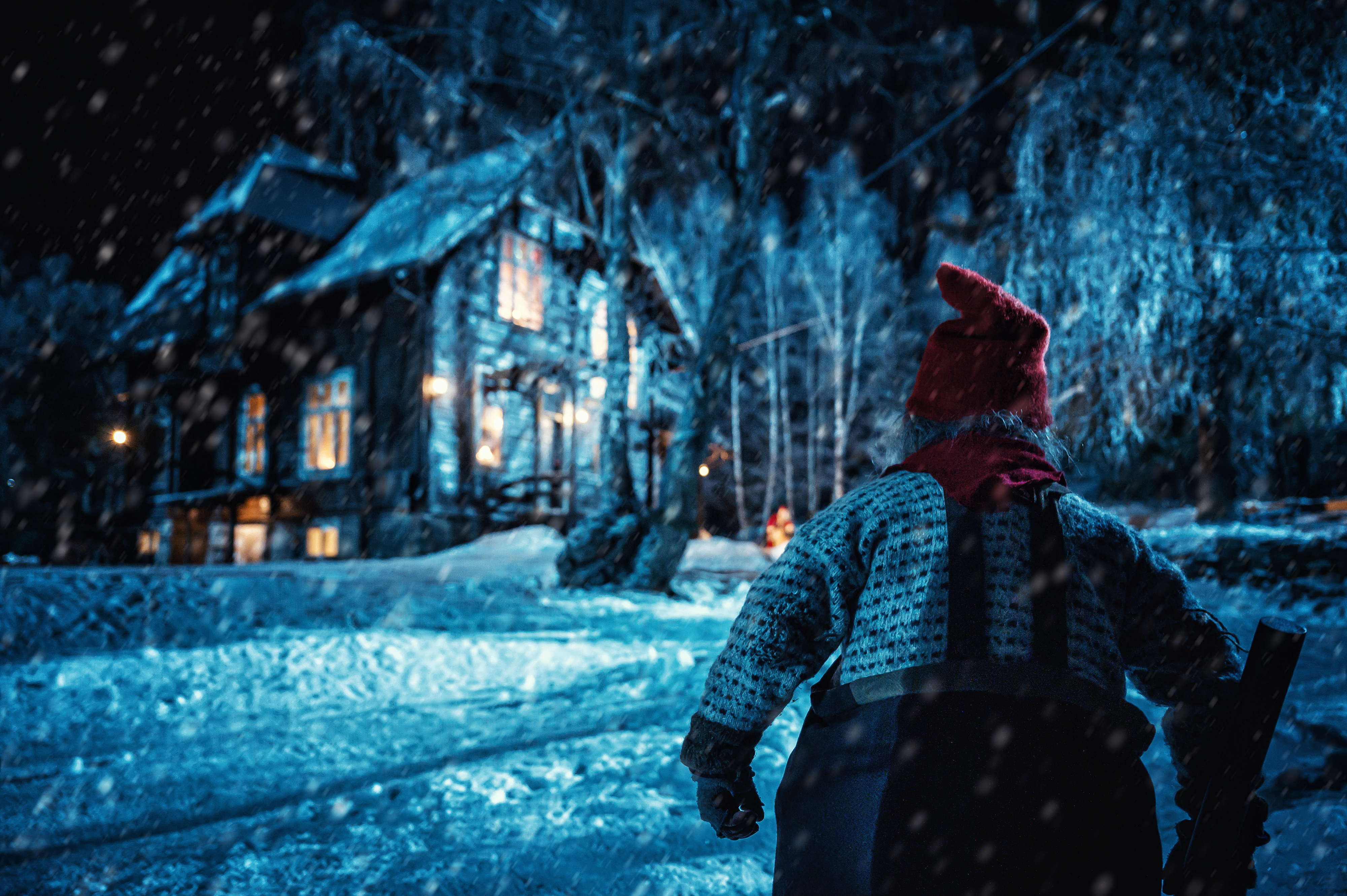 foto. nisse med ryggen til på vei inn mot et stort hus, blåmørke og snø i bildet