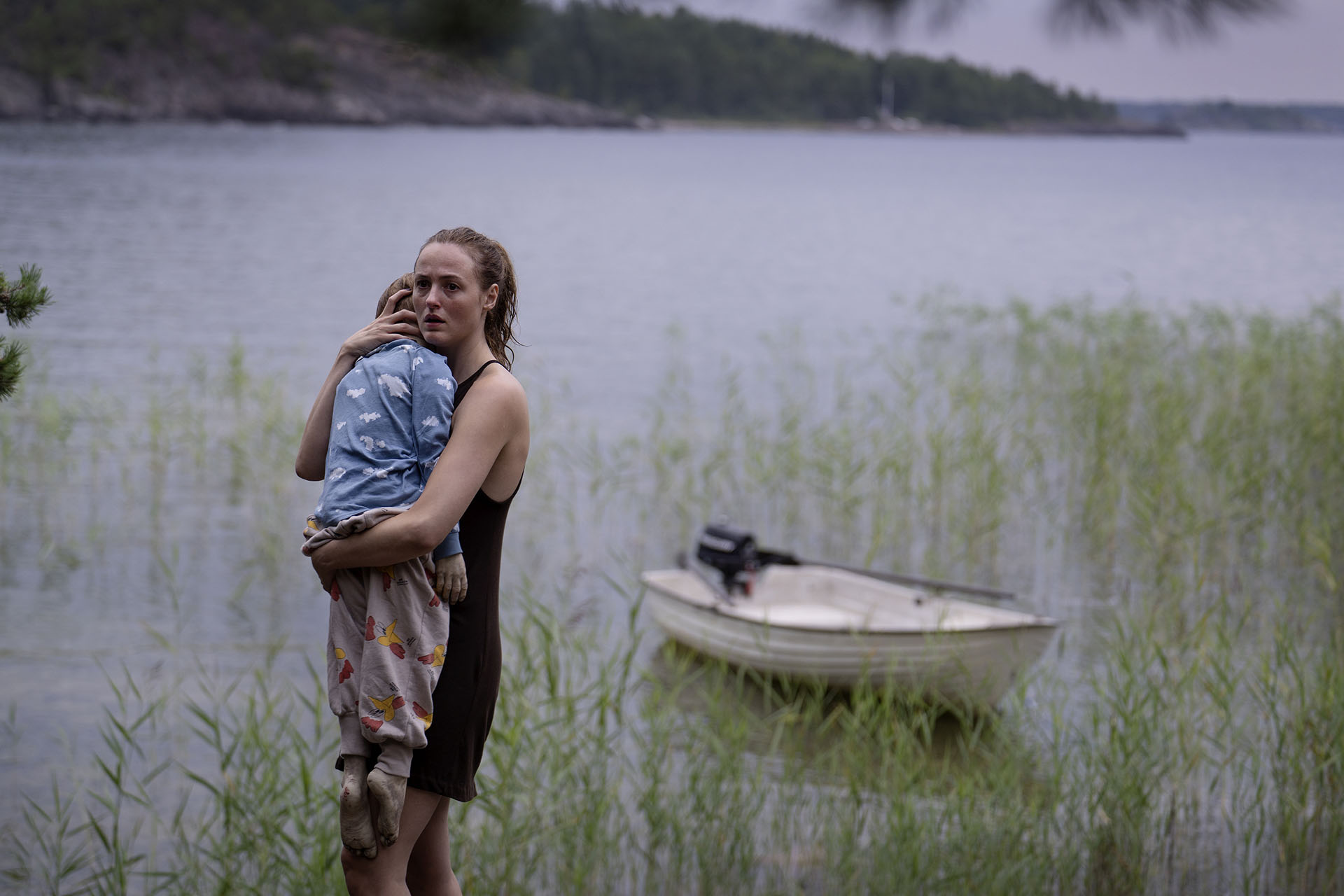 foto. kvinne i singlet står i døråpning og holder seg for munnen med en hånd.