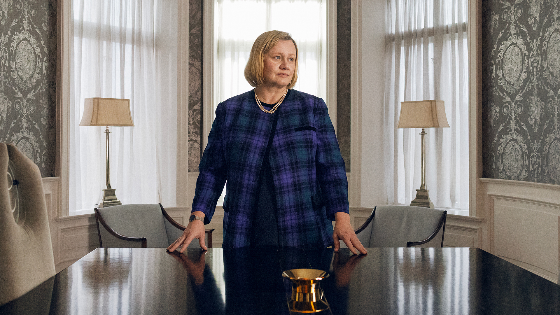 Foto. Kvinne i blå og sort rutete blazer står bak en pult