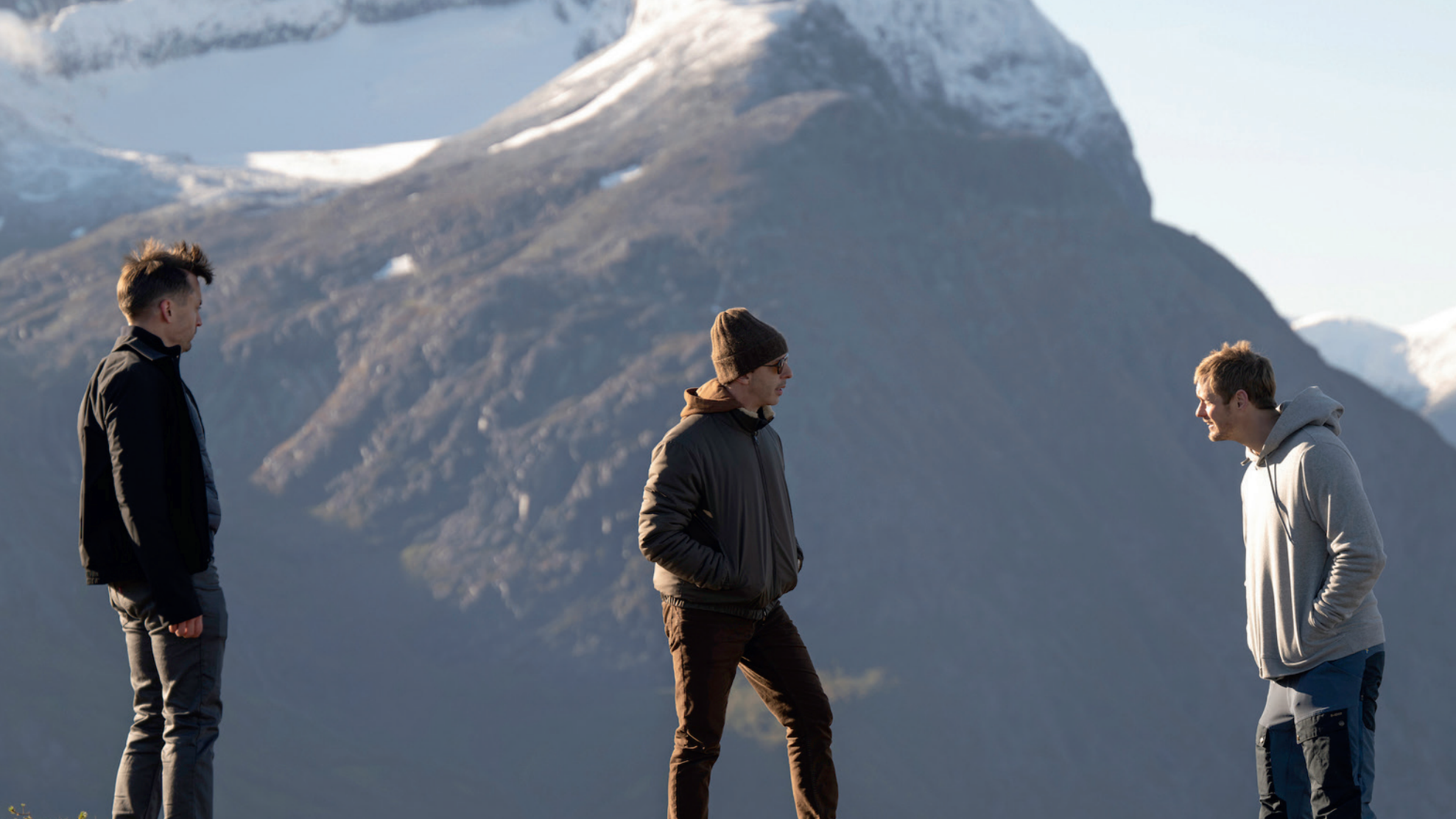 Foto: Tre menn snakket på toppen av et fjell med flere fjell i bakgrunnen