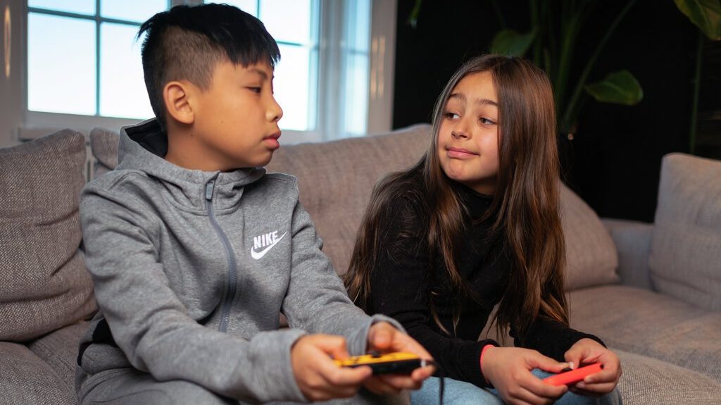 En gutt og jente spiller dataspill sammen i en sofa.
