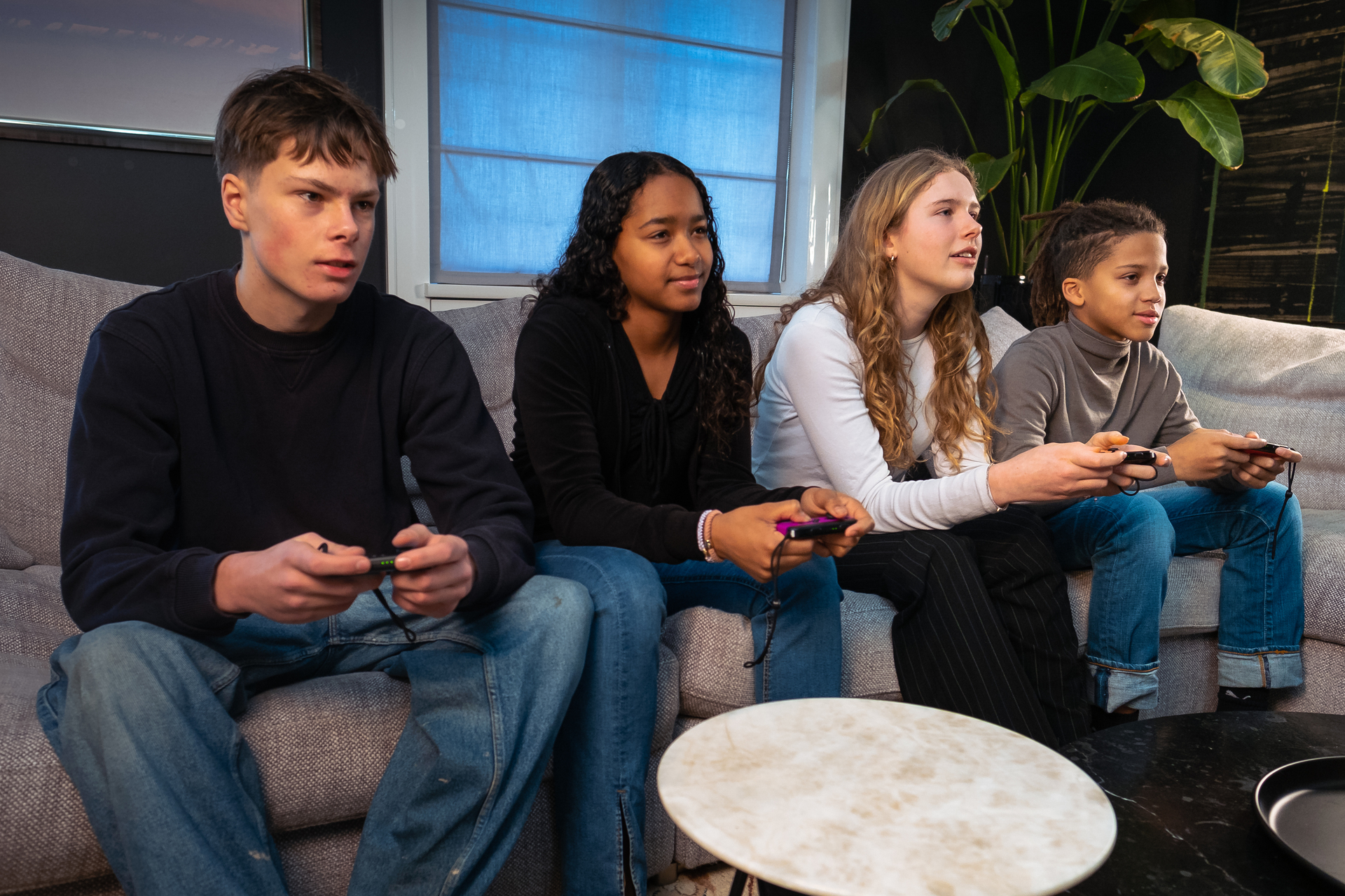 Fire unge sitter på en sofa og spiller sammen. Alle har en Nintendo Switch-kontroller i hendene sine, og stirrer ut av bilderammen.