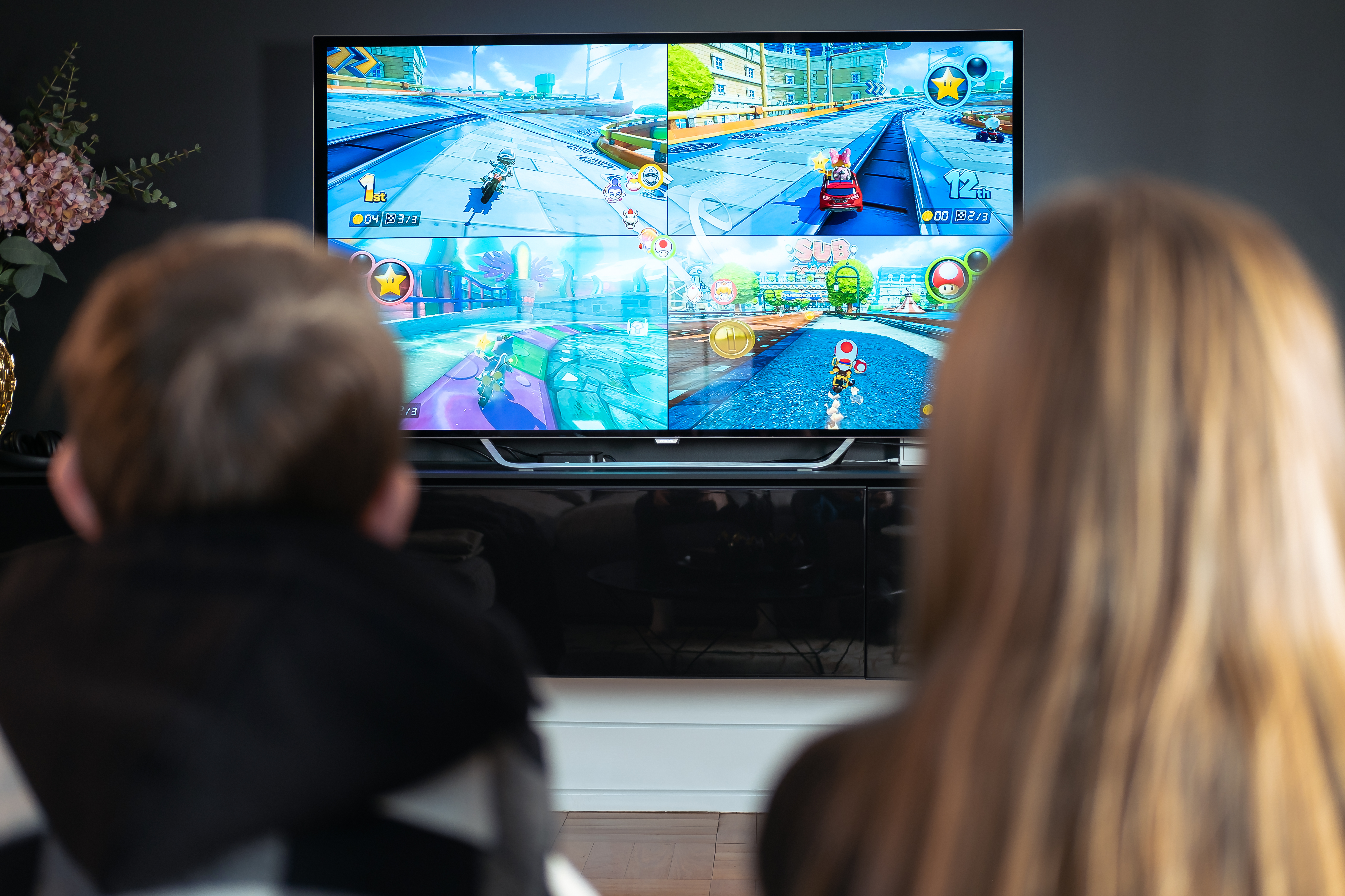 foto. bakhode av to personer som spiller Mario Kart på tv-skjerm