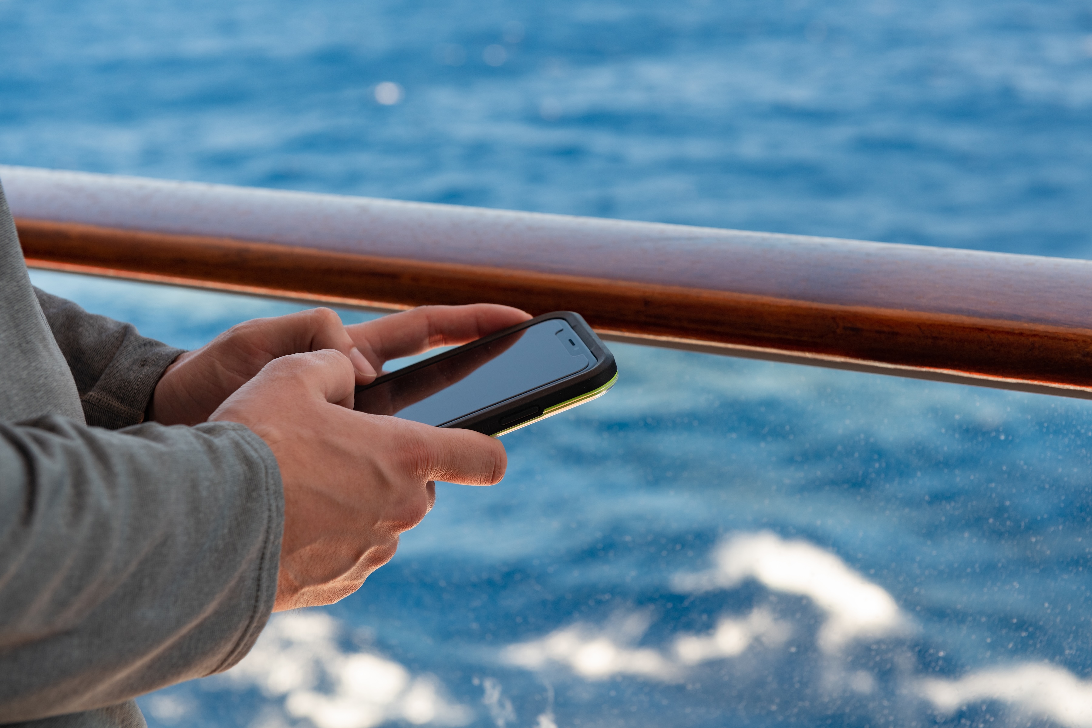 man holds smartphone by cruise ship balcony railing