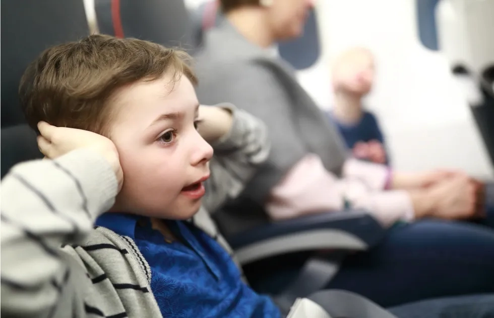 A child presses his hands over his ears on an airplane.