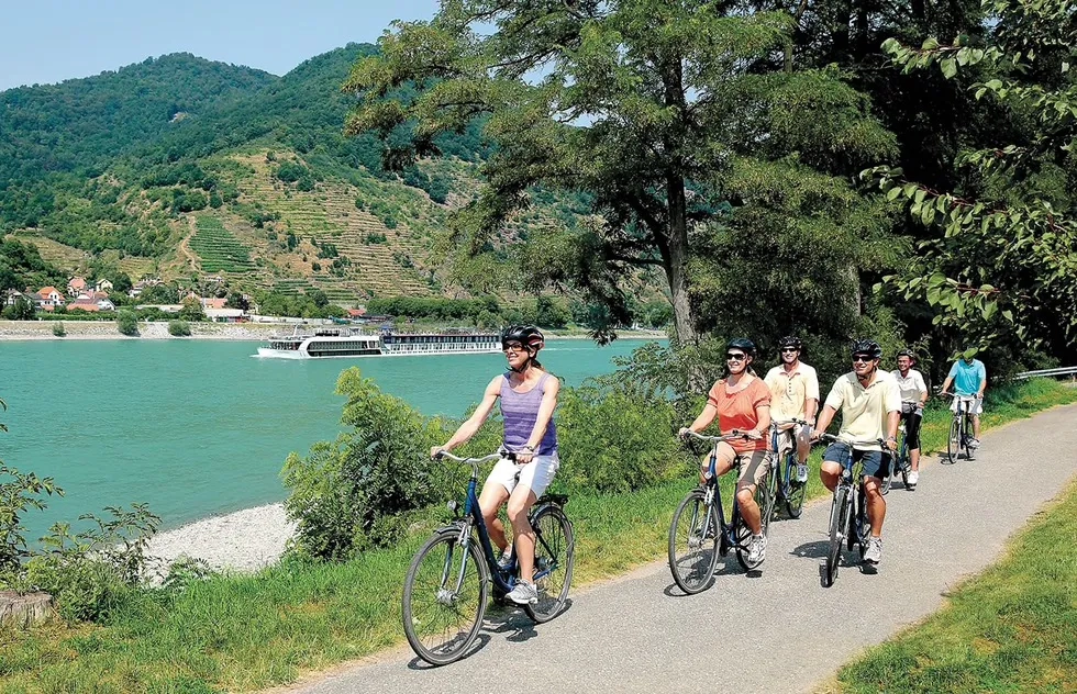 Family cycling on Danube shore with river cruise in background