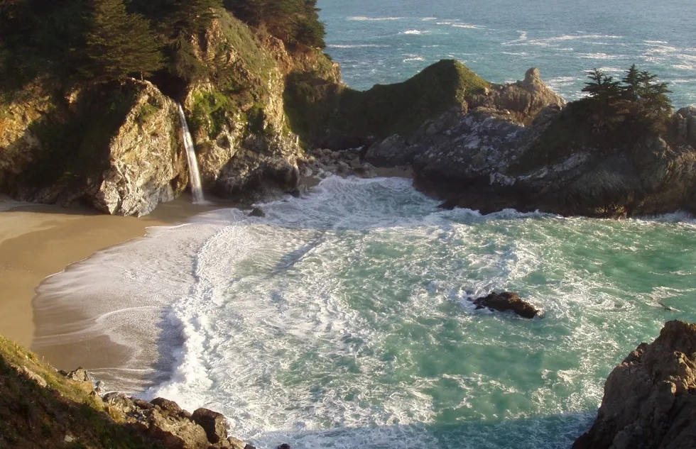 Water swirls amid cliffs and sand in a scenic cove along California's Big Sur coast