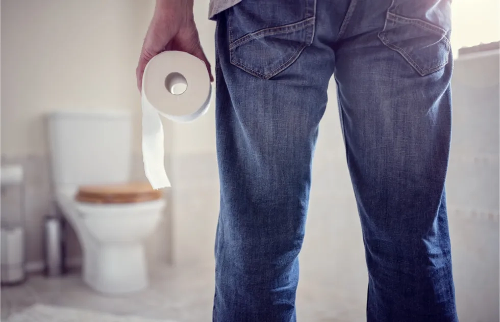 person holding roll of toilet paper and facing toilet from across room