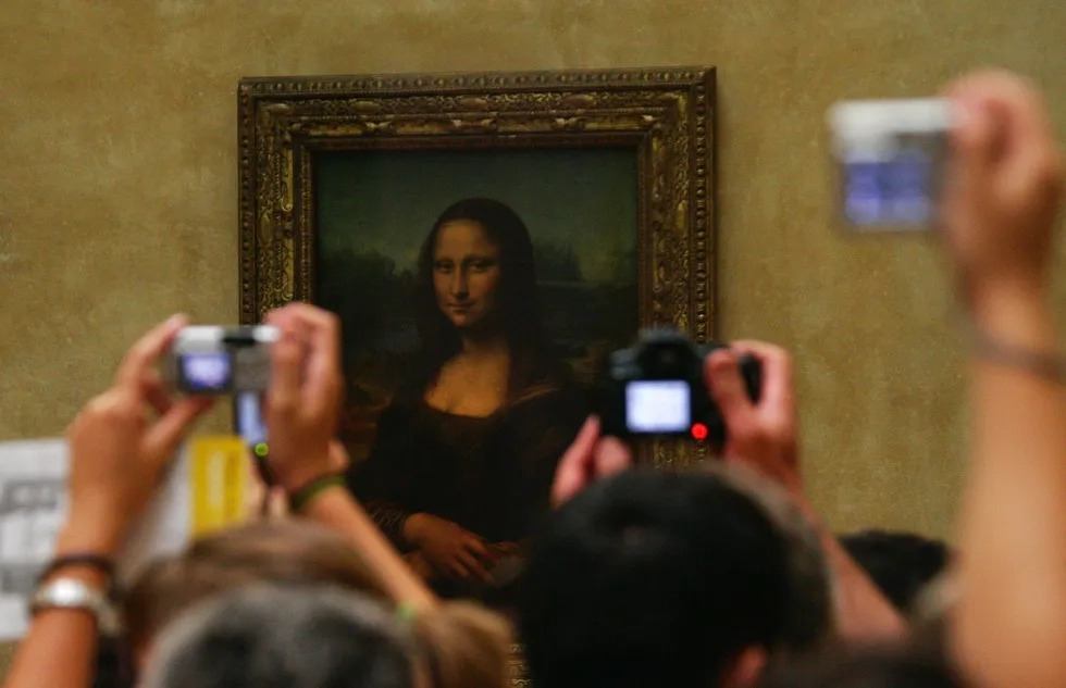 Tourists hold up cameras to photograph the Mona Lisa in the Louvre in Paris