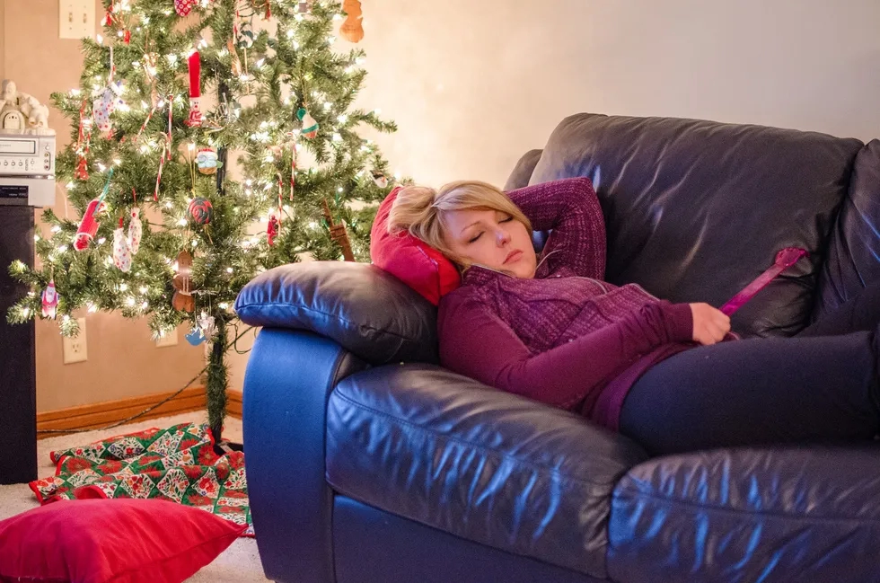 A woman naps on a couch in front of a Christmas tree