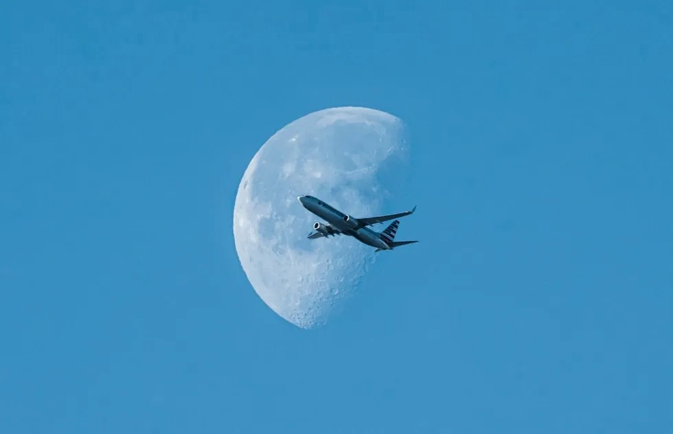 Airplane flying in front of half moon by day
