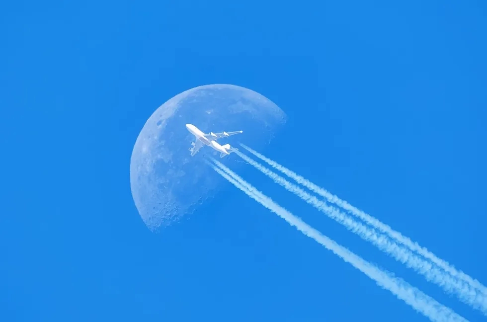 airplane flying in front of moon during daytime
