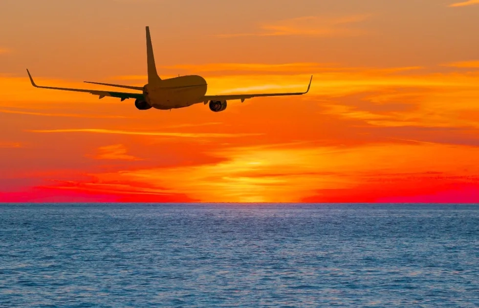 jet airplane flies over water into sunset