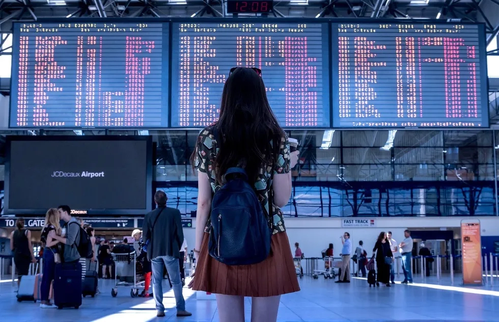 Woman stands in front of airport depatures board