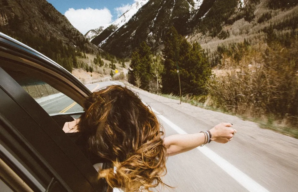 passenger stretches hand out car window on road in mountains