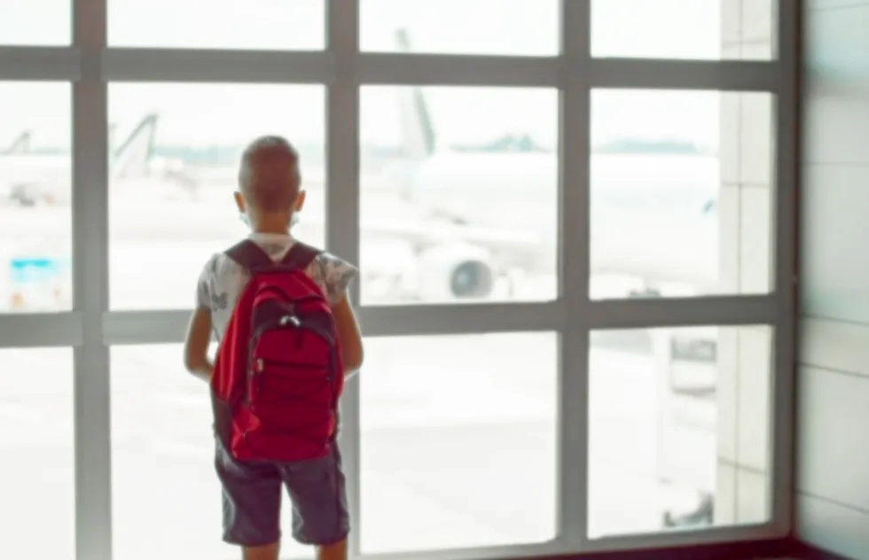 solo child staring out airport window at plane