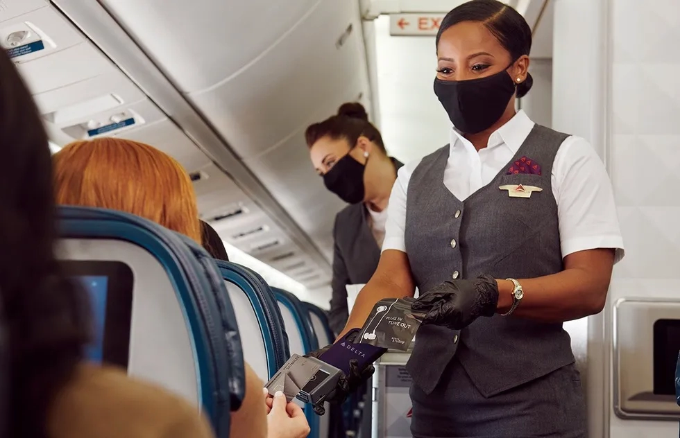 posed shot of passenger making contactless credit card payment with masked flight attendant