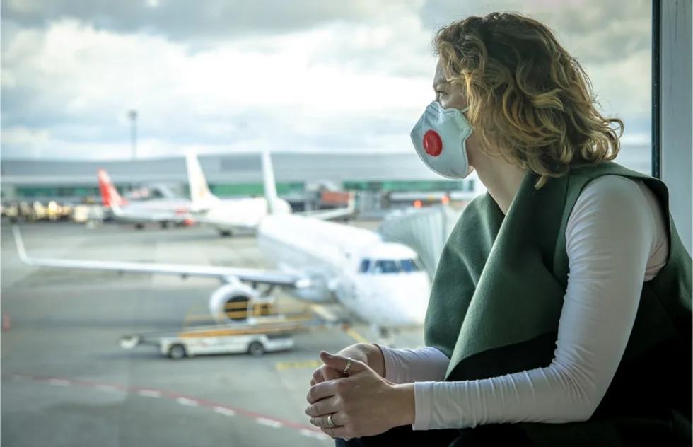 woman in face mask at airport gate looking at planes