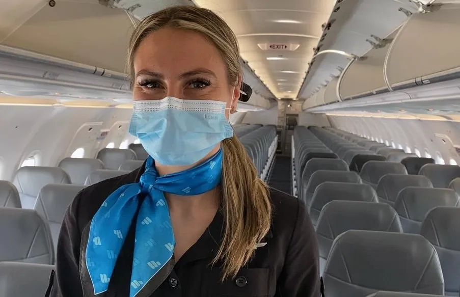 Mask-wearing Frontier Airlines flight attendant in aisle of empty plane