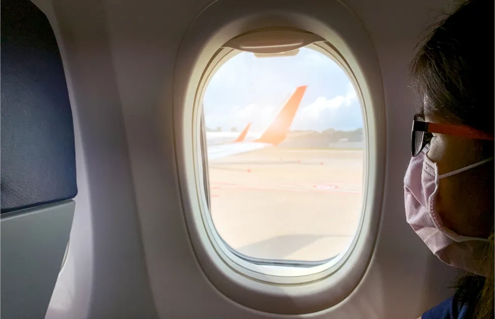female airplane passenger wearing medcial mask looks out window at tarmac