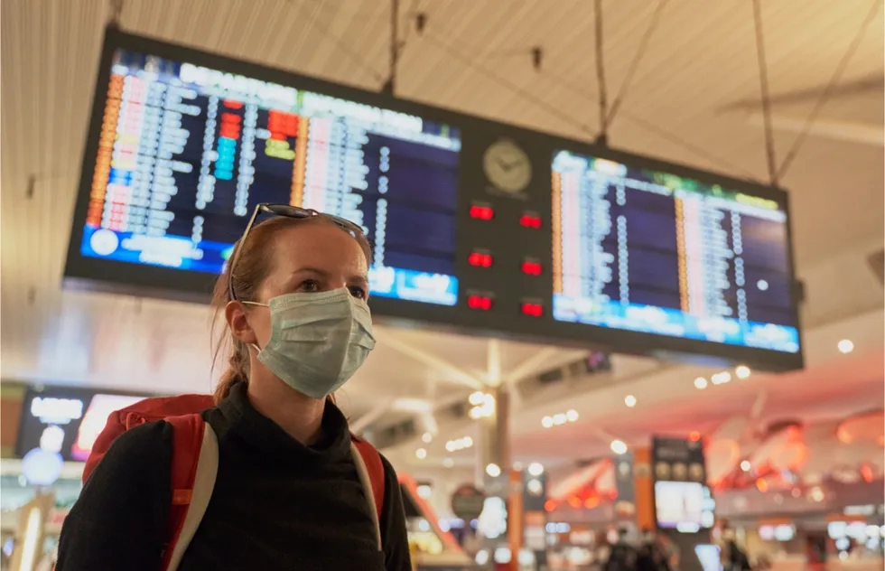 masked passenger under airport departures board