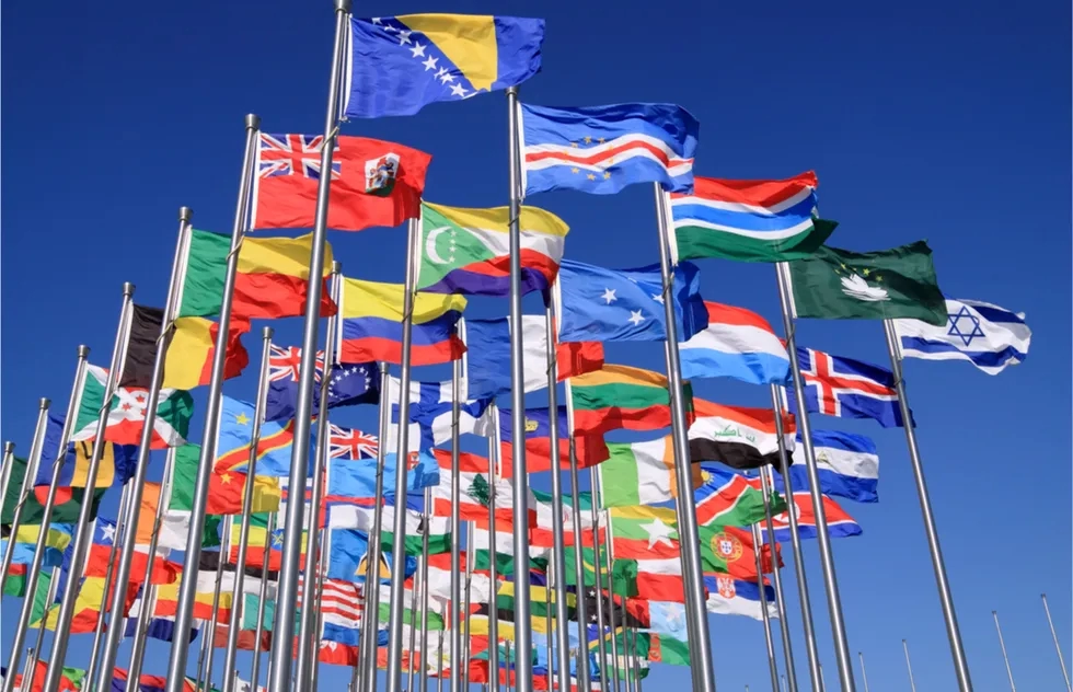 dozens of national flags flying against blue sky atop their own flagpoles